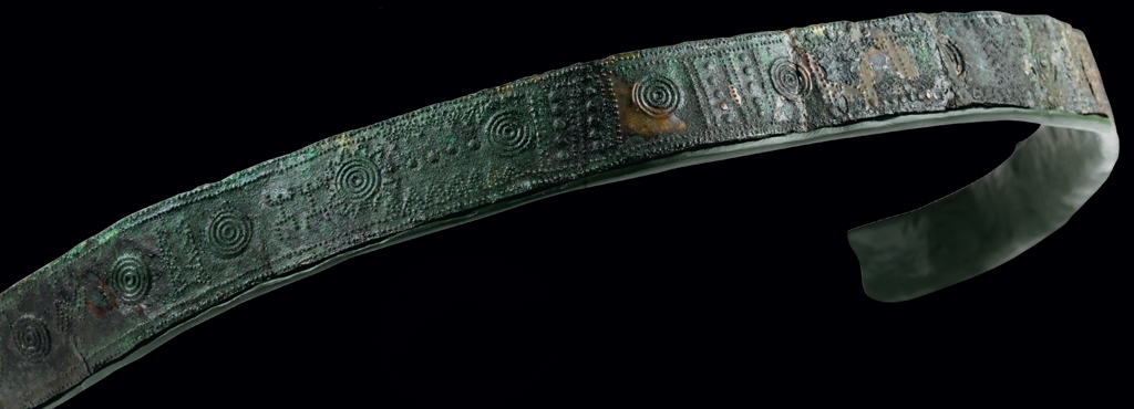 Close up of a bronze belt with curved, spiral, knobs dots and rings in relief with hook and eyes