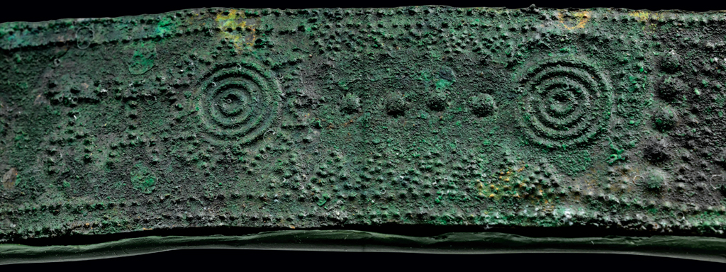 Close up of a bronze belt showing a starburst and figure