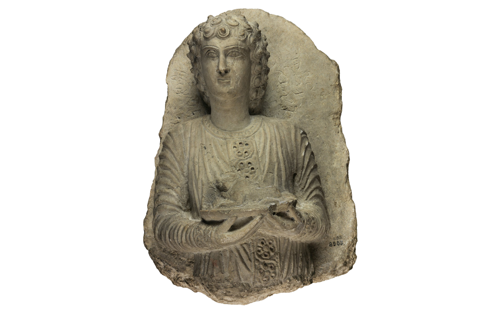 In high relief, young man (bust) with lamb on a tray, Palmyrene inscription to the right and left of his head.